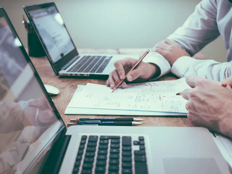 Deux personnes annotent un plan sur papier devant des ordinateurs portables